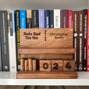 May include: A wooden bookshelf calendar with the text "Books Read This Year" and "Christopher Smith." The calendar displays the number "024" on wooden blocks. The background features a shelf of books.