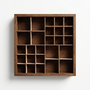 Puede incluir: Un expositor cuadrado de madera con acabado marrón oscuro. La caja está dividida en compartimentos de varios tamaños, creando un patrón de rejilla. Los compartimentos están vacíos y se puede ver la veta de la madera.