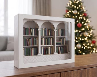 Puede incluir: Un marco rectangular blanco tipo caja con una estantería de tres arcos. El interior contiene filas en miniatura de libros de varios colores, incluyendo verde, azul y rojo, dispuestos en tres niveles con un panel base estampado.