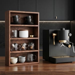 Op de afbeelding: Een houten rek toont zwarte koffiekopjes, heldere glazen en kleine kommen. Een zwarte espressomachine met gouden accenten staat op een houten oppervlak. De achtergrond toont donkere kasten en een marmeren aanrecht.