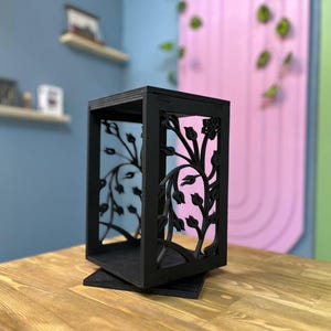 以下が含まれることがあります： 花柄がくり抜かれた黒い木製の装飾箱。箱は木製の表面の上に置かれています