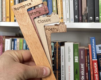 May include: A set of four L-shaped wooden bookmarks with laser-engraved text. The bookmarks feature the words Romance, History, Classic, and Poetry, each topped with a small silhouette icon representing the genre, in varying shades of light and dark wood.