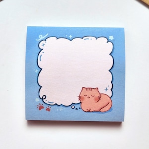 Op de afbeelding: Een blauwe sticky note met een witte wolk en een roze kat erin. De kat slaapt en heeft een kleine roze pootprint ernaast.