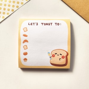 May include: A yellow notepad with the text "Let's Toast To:" and a cartoon illustration of a slice of bread holding a glass of champagne. The notepad has a list of different types of bread on the left side.