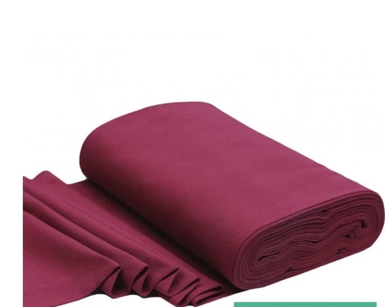 May include: A roll of deep burgundy fabric. The fabric is folded and rolled up, showing the texture of the material.