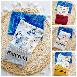 Könnte beinhalten: Eine Sammlung wiederverwendbarer Kühlpacks mit dekorativen Stoffbezügen. Die Bezüge zeigen Wintertier- und Feiertagsmuster, darunter Pinguine, Eisbären und der Weihnachtsmann. Die Texte "BEULENTRÖSTER" und "TROSTSPENDER" sind aufgedruckt.