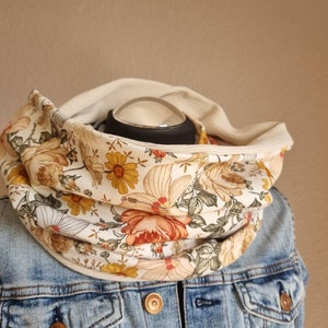 Può includere: Una sciarpa infinita bianca con stampa floreale con fiori gialli, arancioni e verdi. La sciarpa è realizzata in un tessuto morbido ed elastico ed è perfetta per aggiungere un tocco di stile a qualsiasi outfit.