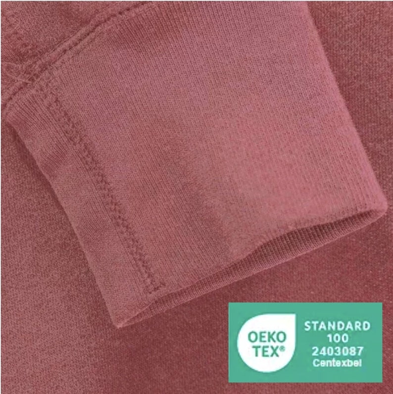 May include: Close-up of a burgundy colored fabric with a stitched seam. The fabric has a soft, textured surface. A green Oeko-Tex Standard 100 certification label is visible in the bottom right corner. The label has the text "OEKO-TEX&reg;" and "STANDARD 100" in white. The number "2403087" and the word "Centexbel" are also visible in white.