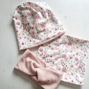 Könnte beinhalten: Ein Set aus drei pink- und weiß gemusterten Stoffen mit Blumenmuster. Das Set beinhaltet eine Mütze, ein Stirnband und ein größeres Stück Stoff, das als Schal oder Decke verwendet werden kann.