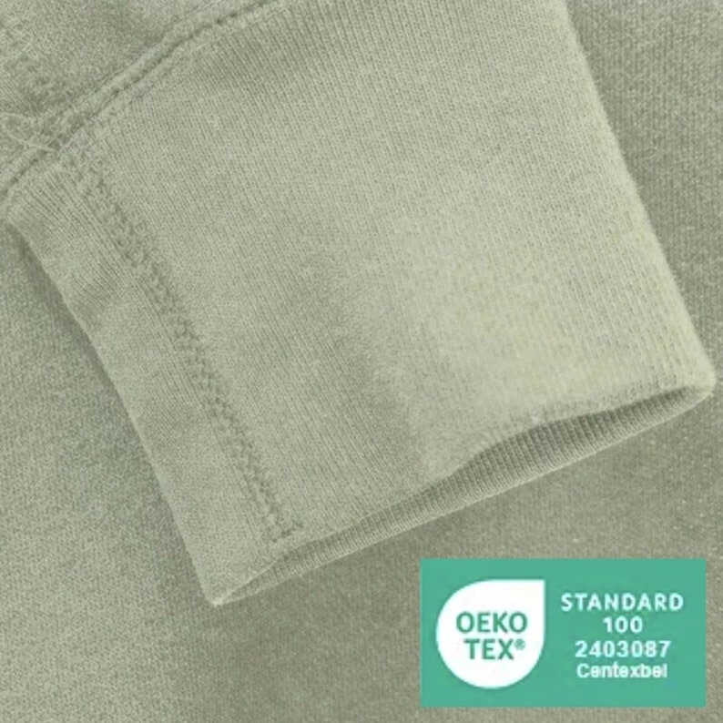 May include: Close-up of a sage green sweatshirt cuff with a sewn-in label that reads "OEKO-TEX&reg; STANDARD 100 2403087  Centexbel".
