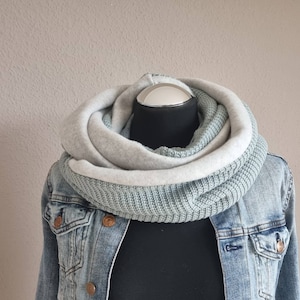 Könnte beinhalten: Ein hellblauer und grauer Infinity-Schal mit Strickstruktur. Der Schal wird auf einer Puppe getragen und ist zweimal umgeschlagen.