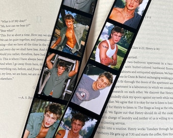 Op de afbeelding: Een zwart-witte fotostrip-bladwijzer met een collage van foto's van een jonge man. De bladwijzer bevat een citaat van A.S. Byatt.