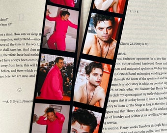 May include: A set of six bookmark photos featuring a man with blue eyes and short brown hair. The photos are arranged in a vertical strip, with the man wearing a pink shirt in some photos and shirtless in others. The photos are printed on a white background with black borders.