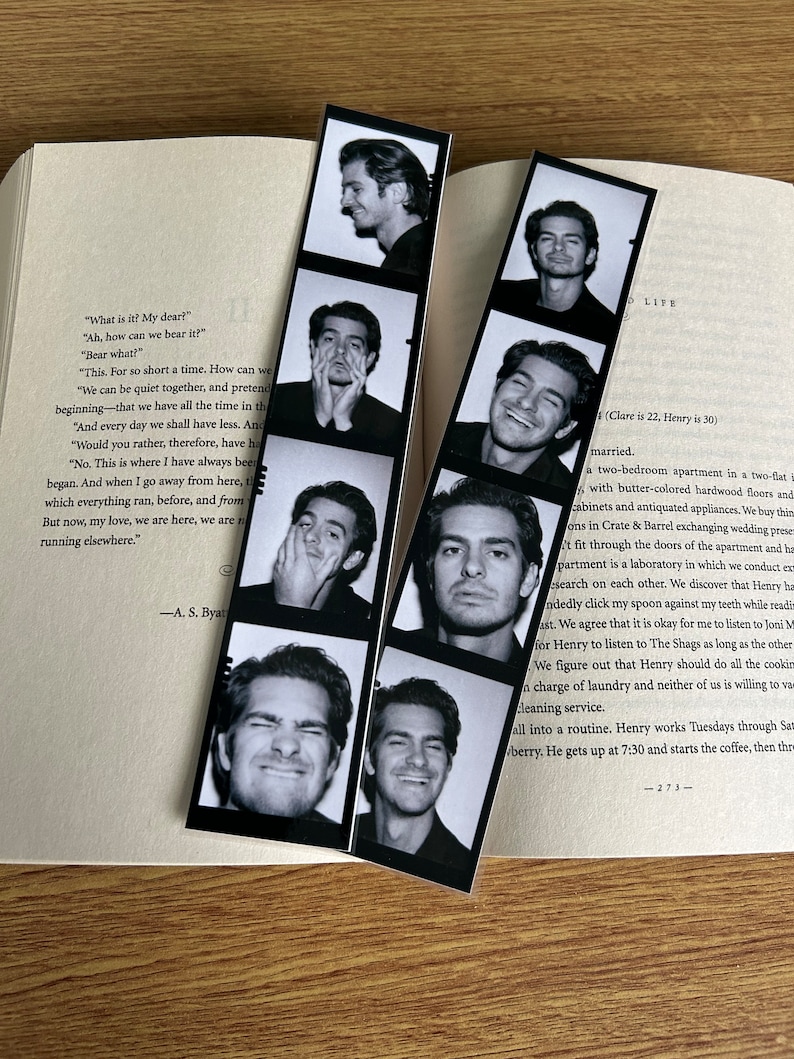 May include: A black and white photo strip bookmark with a man's face in each frame. The man is making different expressions. The bookmark is on top of a book with text about a couple's life together.