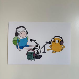 Può includere: Illustrazione di Finn e Jake di Adventure Time che fanno un podcast. Finn, con una maglietta blu e un cappello bianco, e Jake, giallo, indossano le cuffie e sono seduti vicino ai microfoni. Un mixer audio verde e le cuffie sono al centro.