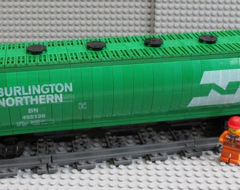 Op de afbeelding: Een groen Burlington Northern modeltreinwagon met zwarte accenten en het BN-logo. Het model bevat de tekst "BURLINGTON NORTHERN" en "BN 455126". Een kleine oranje figuur met een rode helm staat naast de wagon.
