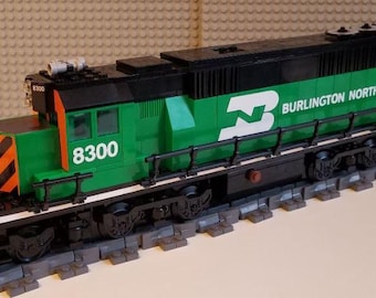 Op de afbeelding: Een groene en zwarte Lego-treinlocomotief met de woorden "Burlington Northern" en het nummer "8300" erop gedrukt. De locomotief staat op een spoor van Lego-stenen.