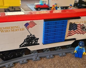 May include: A white and red train car with a blue door and a patriotic design. The car has the text "Remembering All Who Served" and an image of the Iwo Jima Memorial. The car also has a bald eagle and the text "Veteran's Day".