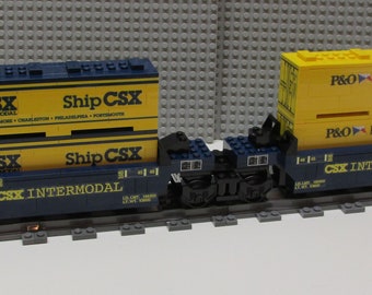 Op de afbeelding: Een blauwe en gele speelgoedtrein met twee goederenwagons. De goederenwagons zijn gelabeld met "CSX Intermodal" en hebben de tekst "Ship CSX" aan de zijkanten. De goederenwagons vervoeren gele containers met het label "P&O Ferrymasters".