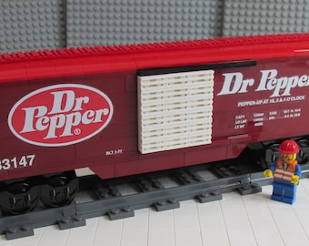 May include: A red and brown Lego train car with the Dr Pepper logo and the words "Pepper-Up at 10, 2 & 4 O'Clock". The car has a white pallet on the side and the number 83147 printed on the side.