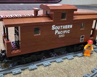 Op de afbeelding: Een bruine houten speelgoedtrein-cabine met een wit label "SOUTHERN PACIFIC 1183". De cabine staat op een grijs plastic treinspoor.
