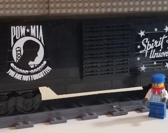 May include: Black Lego train car with white lettering that reads "POW MIA You Are Not Forgotten" and "Spirit of the Union Pacific". The car has a black and white Union Pacific logo and a black and white POW MIA logo. The car is on a Lego track.