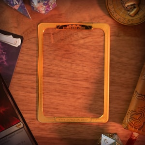 May include: A gold-colored frame with a black background and the text "COMMAND ZONE" and "WWW.DUNGEONSHOP.COM". The frame is on a wooden surface.