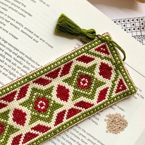 May include: A cross-stitch bookmark pattern featuring a repeating geometric design with red, green, and white stars. The bookmark is titled "Wish Upon A Star" and includes a link to the pattern on the website "ancientsagedesigns.com".