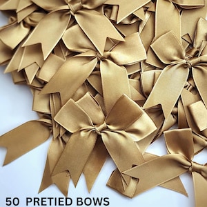 May include: A pile of 50 gold satin pre-tied bows. The bows are arranged in a random pattern and are all the same size. The text "50 PRETIED BOWS" is printed on the bottom of the image.