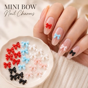 May include: Mini Bow Nail Charms featuring small, three-dimensional bow-shaped decorations in red, light blue, white, pink, and black. These charms are displayed on a small scalloped dish and applied to fingernails with a clear base coat.