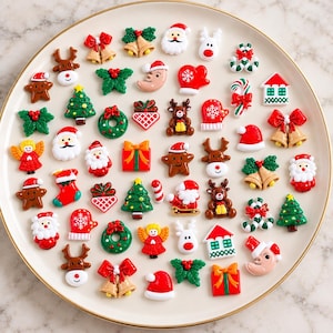 May include: A collection of small, colorful Christmas-themed resin cabochons arranged on a round plate. The set includes figures of Santa Claus, reindeer, gingerbread people, Christmas trees, wreaths, bells, gift boxes, stockings, and mittens.