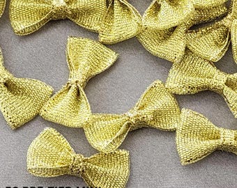 May include: A close-up of 50 gold pre-tied mini bows. The bows are made of a shimmery fabric and are perfect for adding a touch of sparkle to any project.