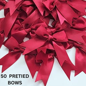 May include: A pile of 50 pre-tied burgundy satin bows. The bows are arranged in a random pattern and are ready to be used for gift wrapping or other decorative purposes.