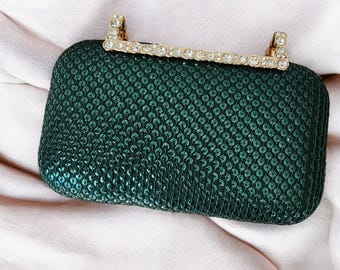 Puede incluir: Un bolso de mano verde oscuro con un cierre adornado con cristales y oro.