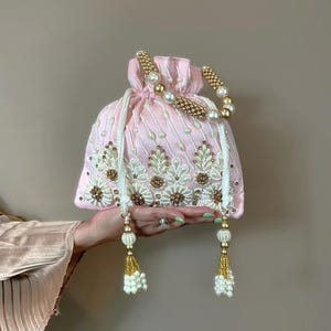 May include: A pink drawstring bag with gold and white beaded embellishments. The bag has a pearl and gold beaded handle and two tassels with pearls.