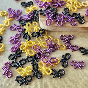 May include: A collection of small, beaded bows in black, yellow, and purple. The bows are scattered on a textured surface.