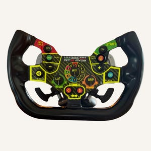 Puede incluir: Un volante de carreras negro con un panel central de fibra de carbono con el texto HURACAN GT3 EVO2. El volante incluye numerosos botones etiquetados, diales giratorios para ajustes de mix, grip y lat, y levas de cambio en la parte trasera.