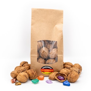 Könnte beinhalten: Eine braune Papiertüte mit einem transparenten Fenster, gefüllt mit Walnüssen. Walnüsse sind um die Tüte herum verstreut, einige sind aufgebrochen und geben das Nussfleisch frei. Bunte Edelsteine sind ebenfalls vorhanden.