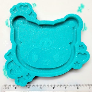 May include: Teal blue silicone mold with a cartoon animal face design. The mold has a heart and star shaped border.