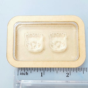 May include: Two clear plastic molds in a wooden frame. The molds are shaped like a cartoon animal with a crown on its head. The frame is about 2 inches wide.