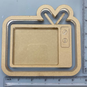 May include: A wooden TV-shaped picture frame. The frame is made of light brown wood and has a retro TV design with an antenna and control buttons. The frame measures approximately 5 inches in height and 5 inches in width.