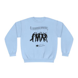 Op de afbeelding: Lichtblauwe trui met een zwart-witte afbeelding van vijf figuren met de tekst "DEFINITELY MAYBE" en "Celebrating 25 Years".
