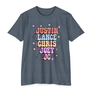Puede incluir: Una camiseta azul pizarra de manga corta con los nombres "JUSTIN", "LANCE", "CHRIS", "JOEY" y "JC" en una fuente retro. Cada nombre tiene un color diferente, con acentos de estrellas. La camiseta tiene cuello redondo.