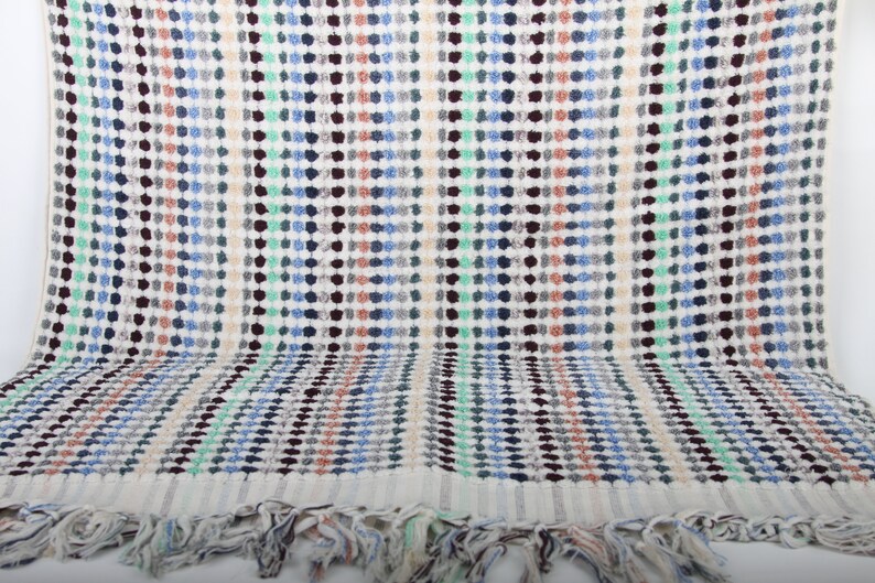 May include: A white bath towel with a colorful geometric pattern of small circles in shades of blue, green, brown, and orange. The towel has a fringe border.