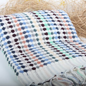 May include: A white bath towel with a checkered pattern in shades of blue, green, brown, and beige. The towel has a fringe border.