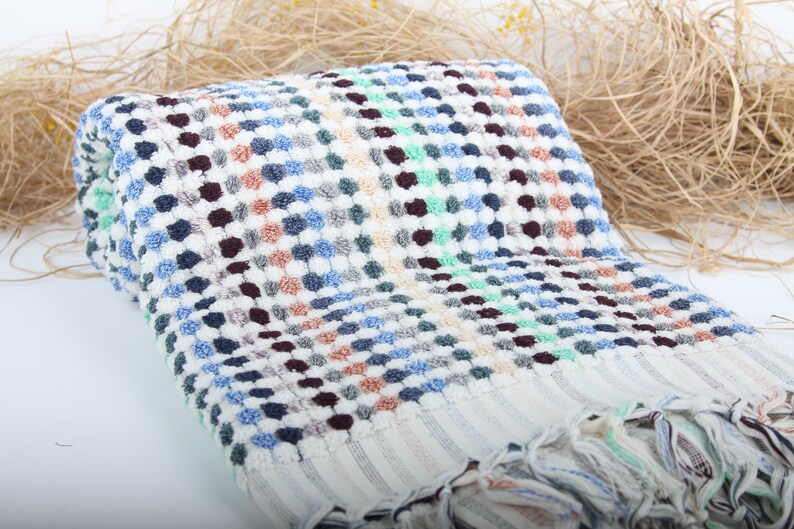 May include: A white bath towel with a checkered pattern in shades of blue, green, brown, and beige. The towel has a fringe border.