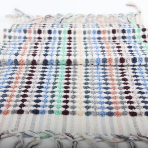 May include: A white hand towel with a colorful geometric pattern of blue, green, red, and brown dots. The towel has a fringe border.