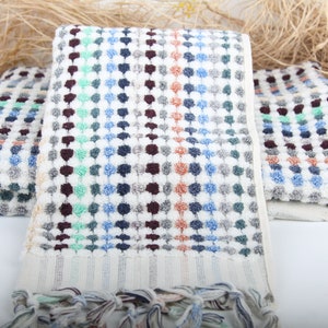 May include: Three white bath towels with a colorful geometric pattern of blue, green, brown, and orange dots. The towels have a fringe border.