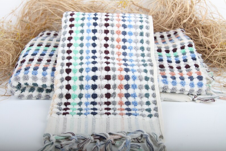 May include: Three white bath towels with a colorful geometric pattern of blue, green, brown, and orange dots. The towels have a fringe border.