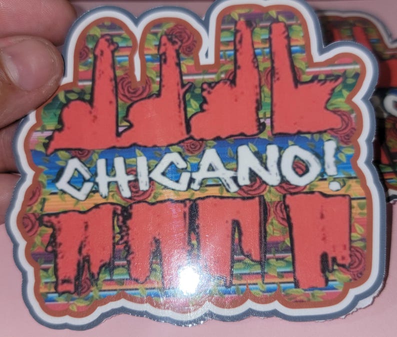 以下が含まれることがあります： 「CHICANO！」の文字が白で、黒い縁取りで描かれたステッカー。カラフルな花柄と幾何学模様の背景。赤、緑、茶色の色合い。ステッカーは手で持たれています。